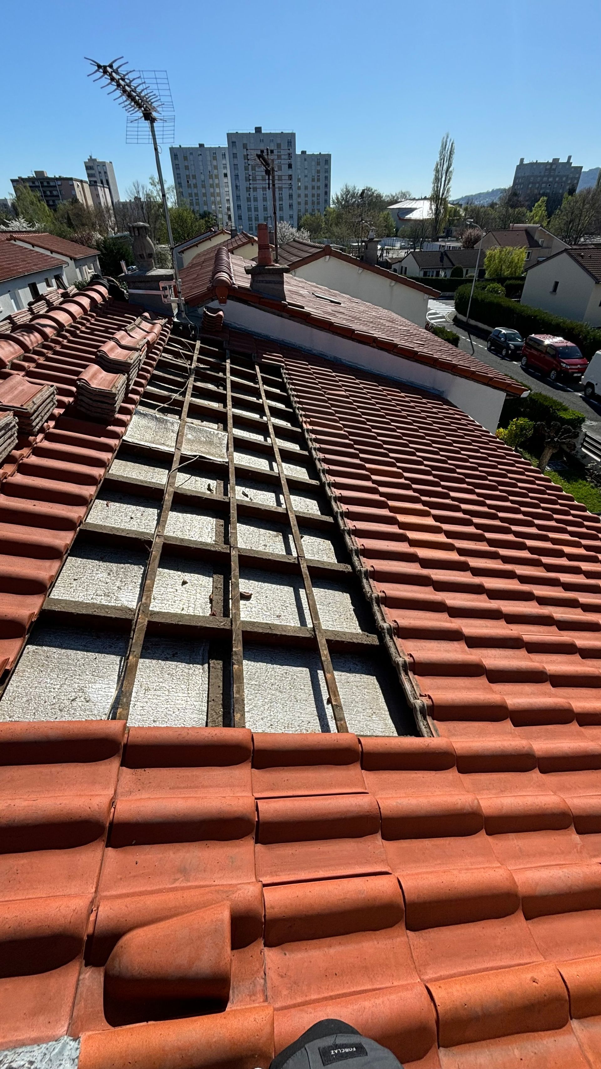 Toiture en tuiles de terre cuite partiellement démontée, laissant apparaître les poutres en bois, en milieu urbain.