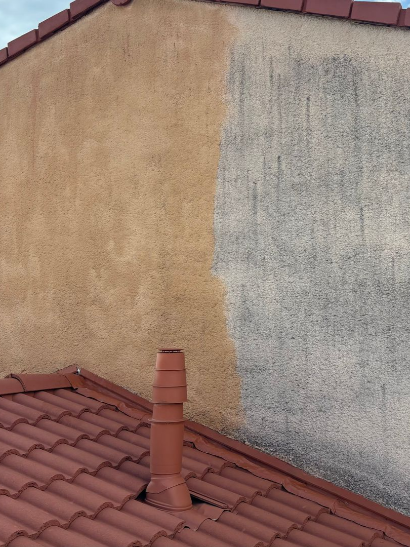 Mur en stuc beige jouxtant une partie grise patinée par le temps ; toit de tuiles rouges et cheminée en dessous.