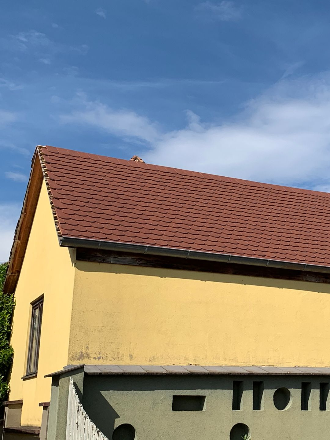 Bâtiment jaune au toit rouge se détachant sur un ciel bleu, partiellement masqué par un mur décoratif.