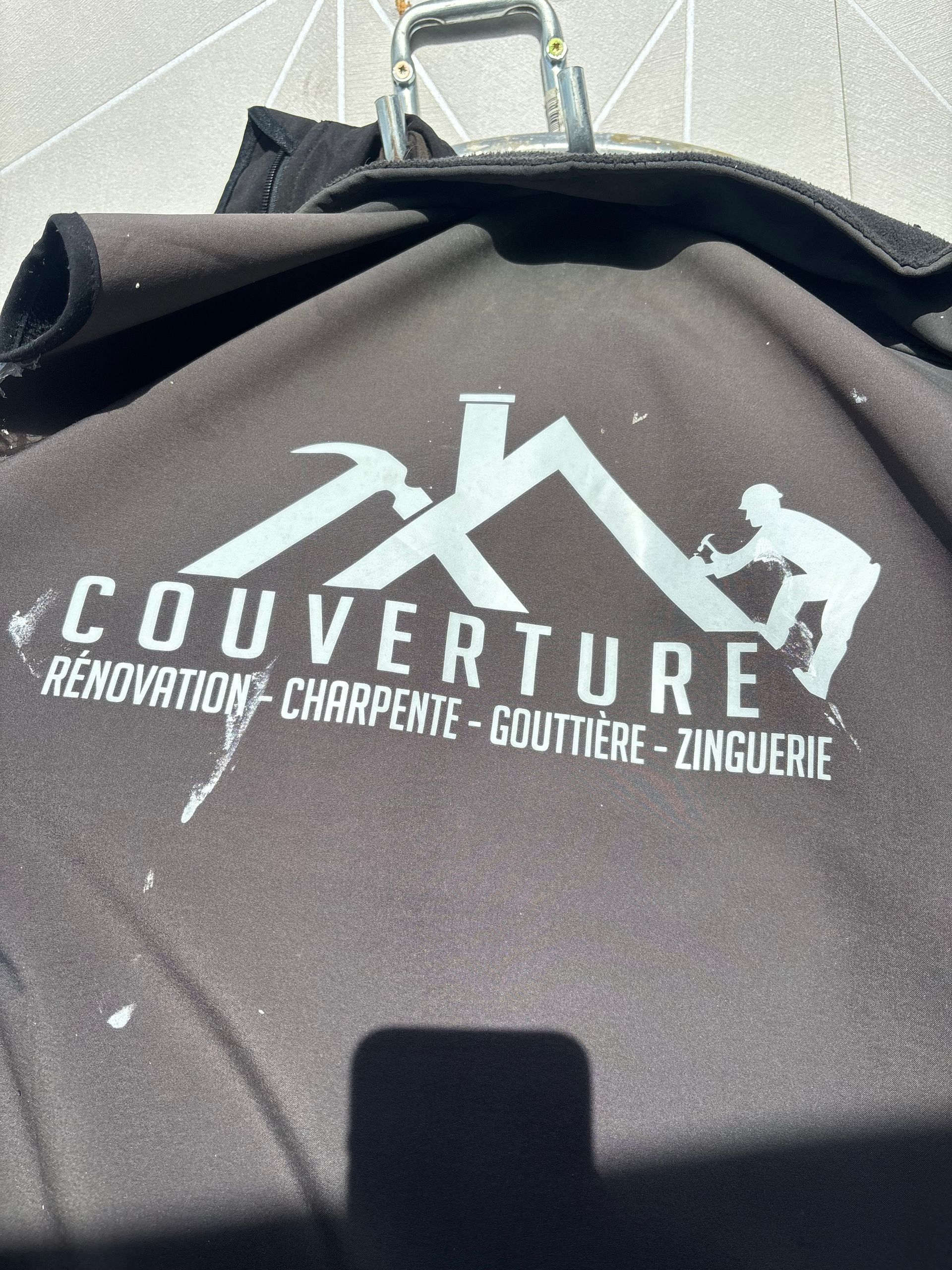 Sac noir avec logo gris : services de toiture, avec la silhouette d’un ouvrier.