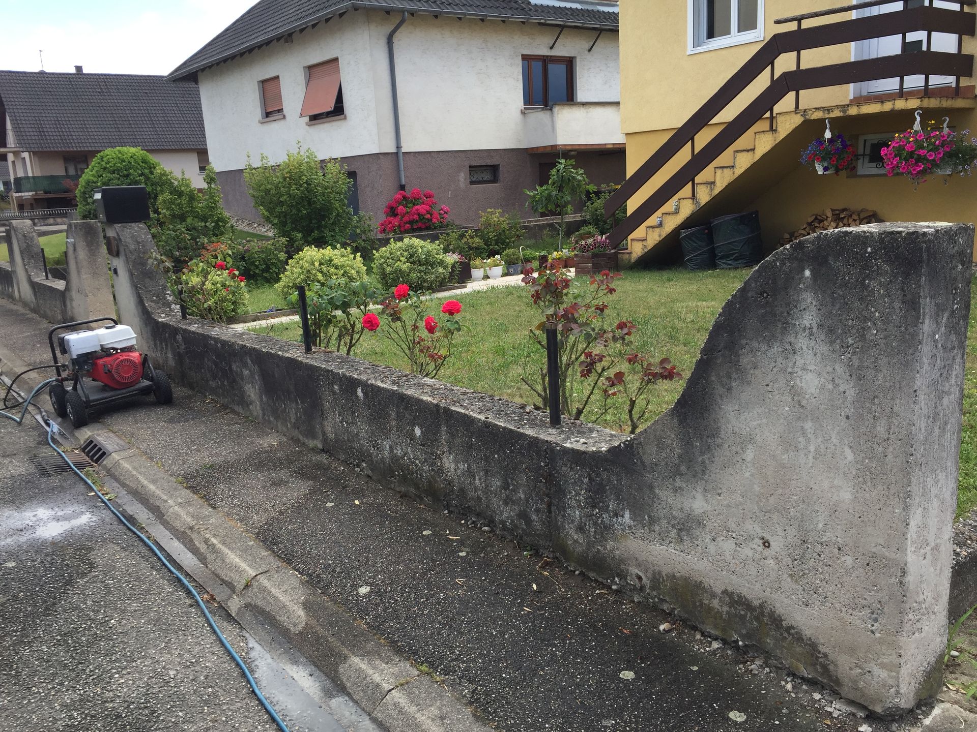 Nettoyage à haute pression d'un mur de soutènement en béton devant une maison.