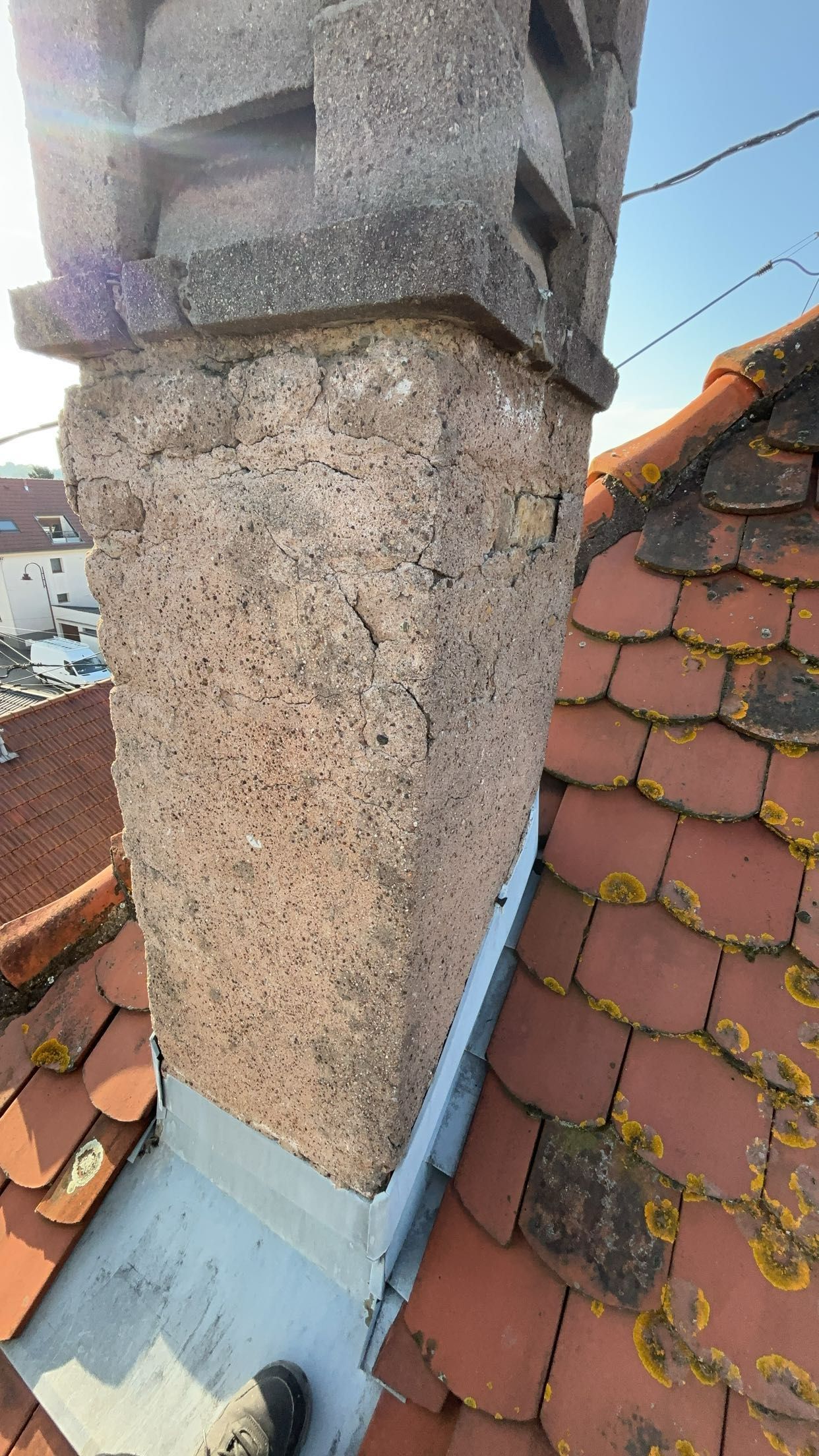 Cheminée sur un toit de tuiles rouges ; gros plan montrant la texture de la pierre et les solins métalliques.