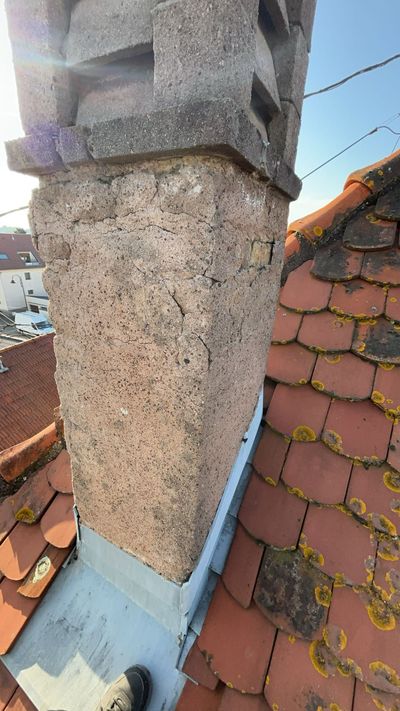 Cheminée sur un toit de tuiles rouges ; gros plan montrant la texture de la pierre et les solins métalliques.