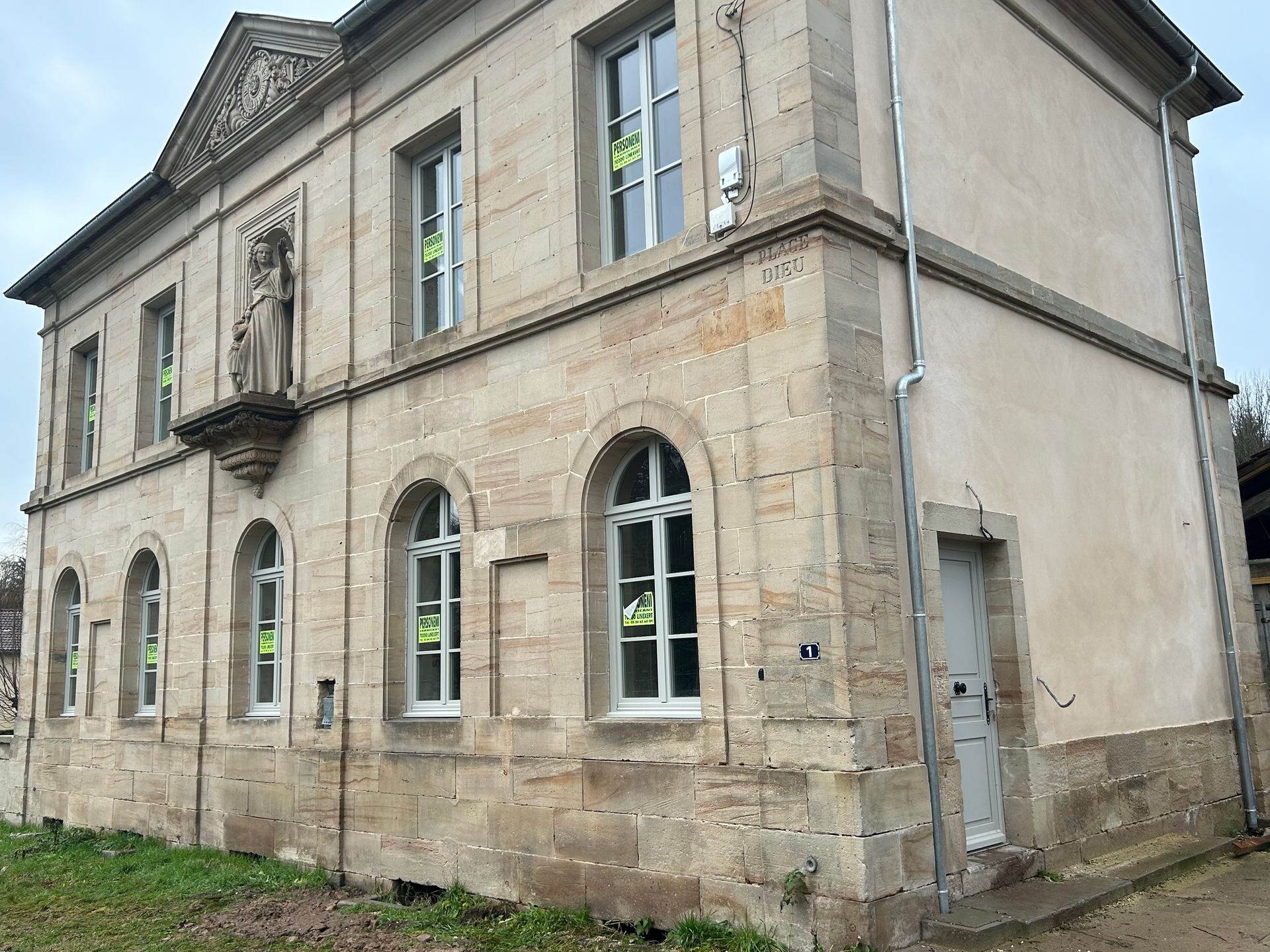 Bâtiment en pierre de deux étages avec des fenêtres cintrées, une statue et de nouveaux encadrements de fenêtres blancs.