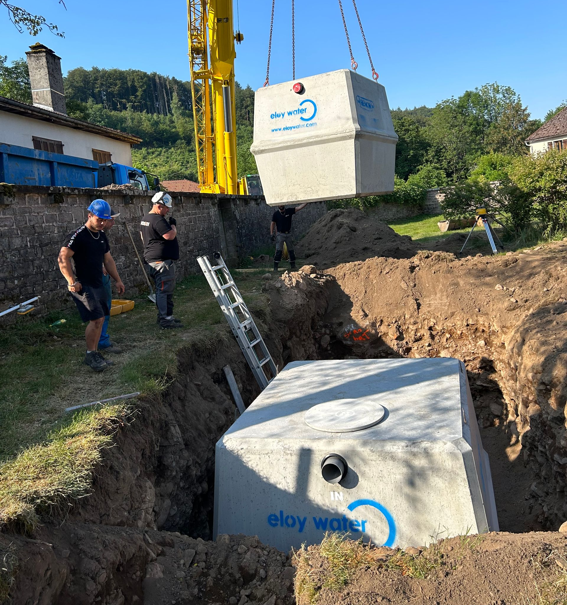 Des ouvriers installent un réservoir d'eau en béton à l'aide d'une grue dans un jardin.