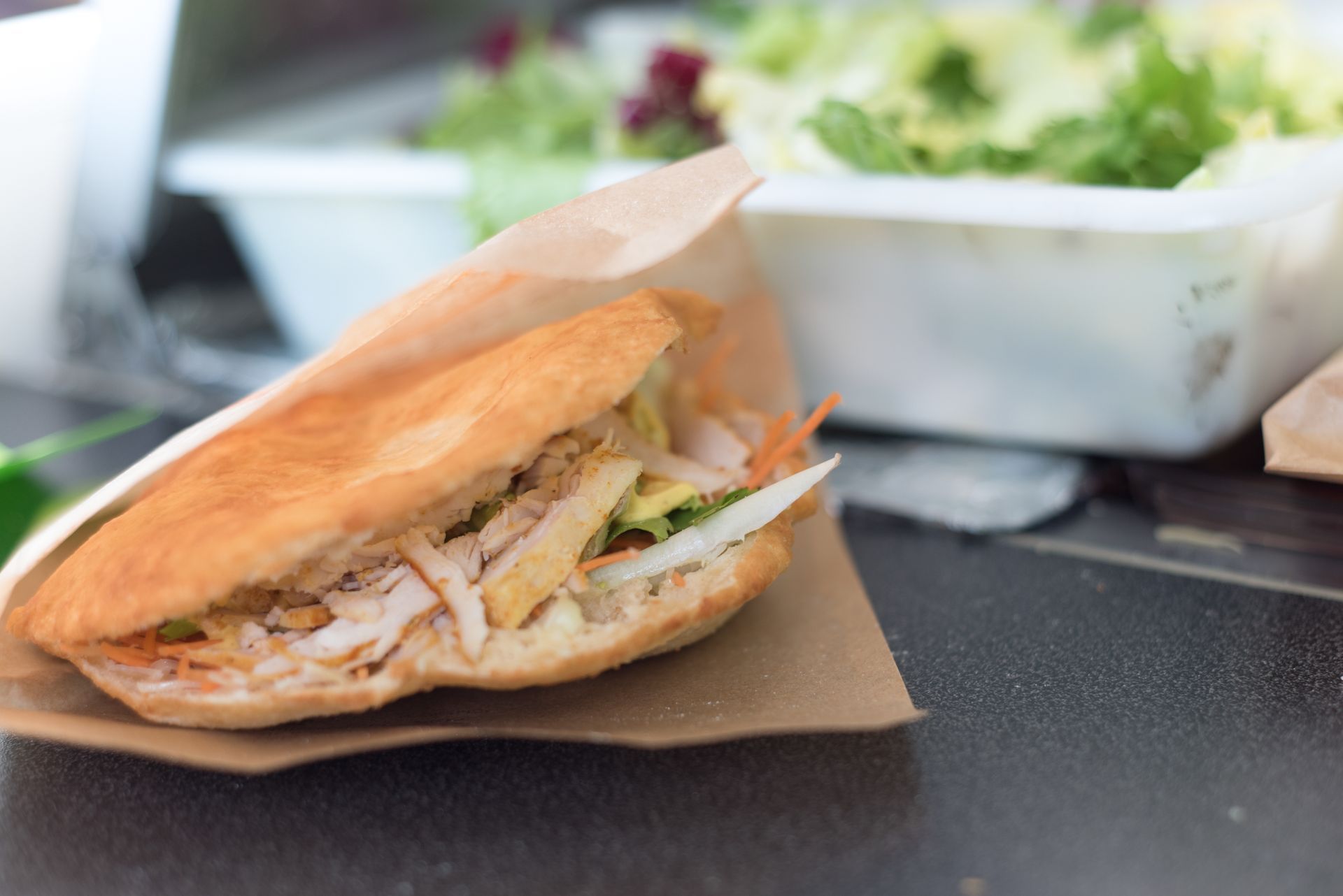 Sandwich garni de viande hachée effilochée, posé sur du papier sulfurisé, à côté d'une salade à emporter.