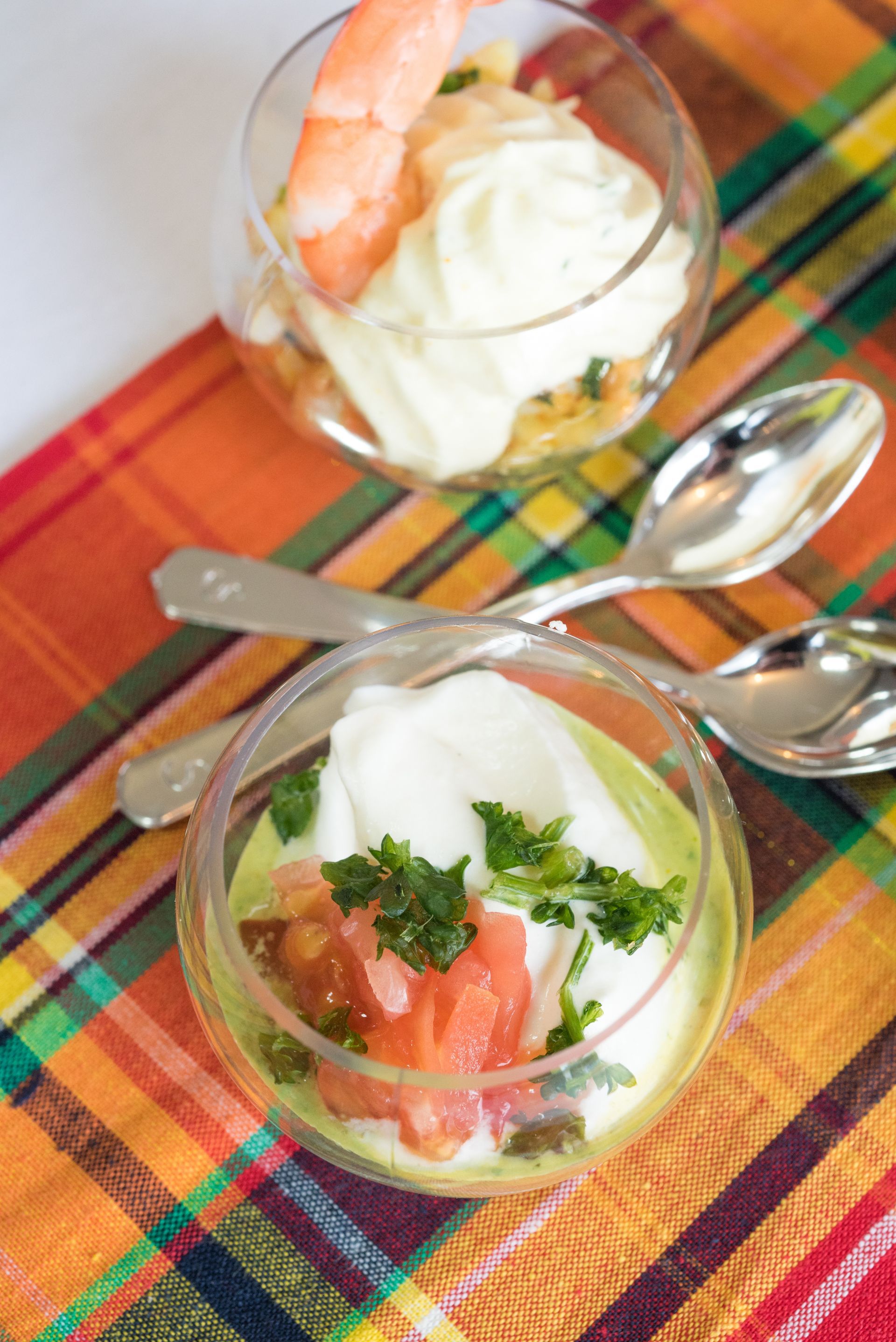 Deux amuse-bouche aux crevettes et à la crème, servis dans des verres sur une serviette à carreaux colorée, avec des cuillères.