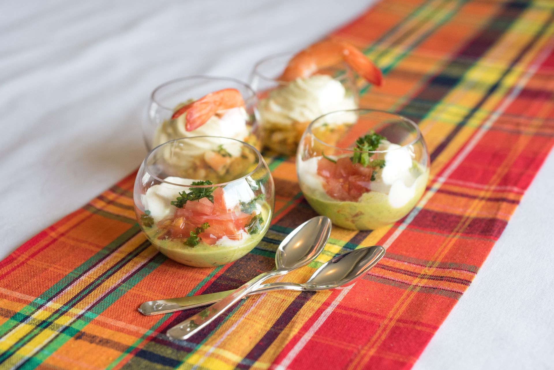 Coupes à dessert en verre contenant des fruits et de la crème en couches, disposées sur une nappe à carreaux colorée.