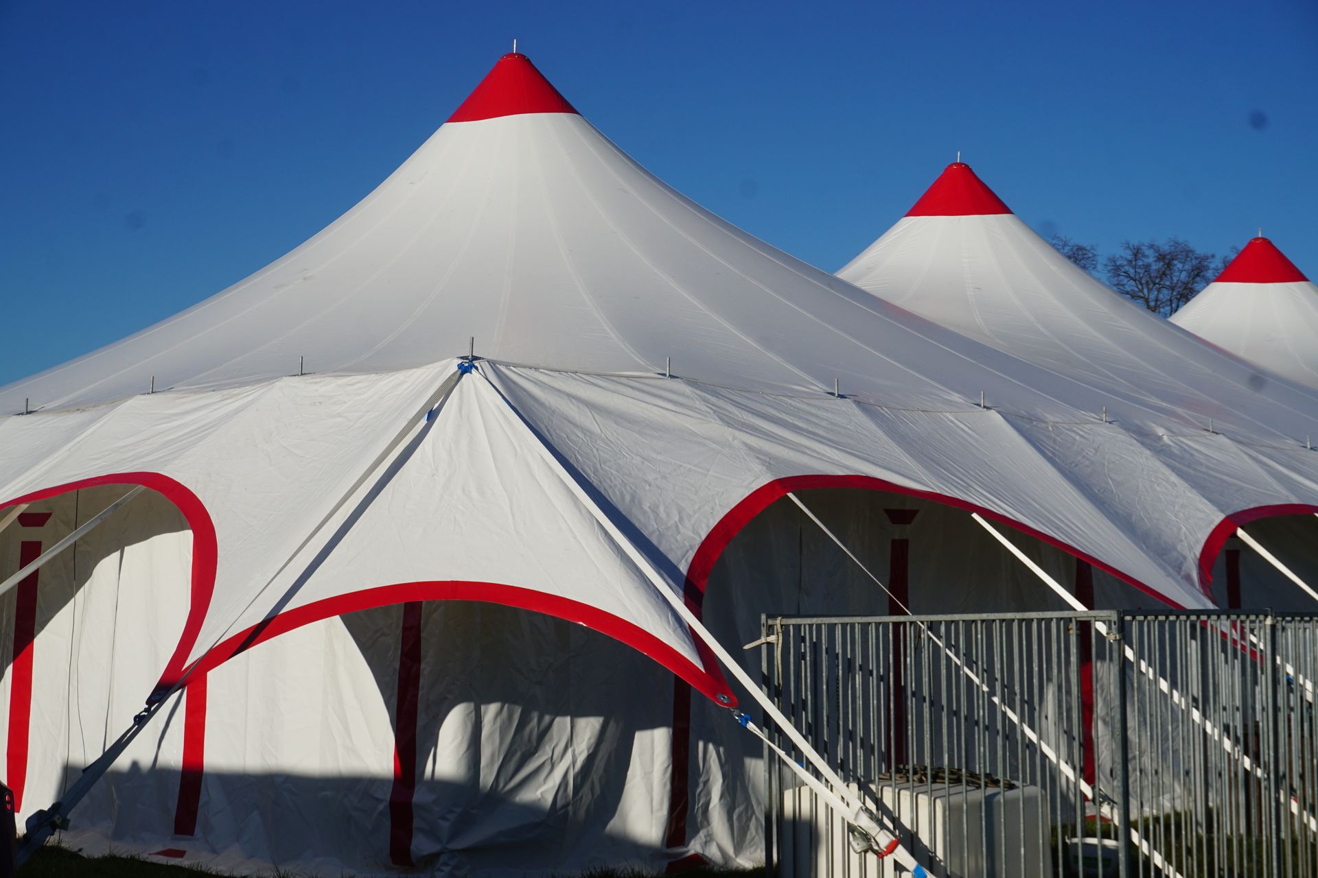 Des tentes blanches à toit rouge, installées derrière une clôture métallique sous un ciel bleu azur.