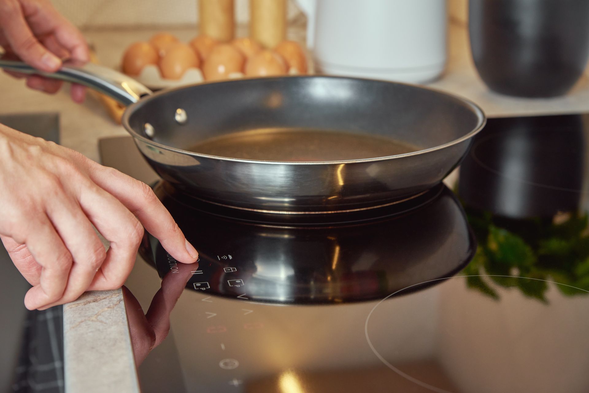 Des mains manipulent une poêle à frire sur une plaque de cuisson dans une cuisine.