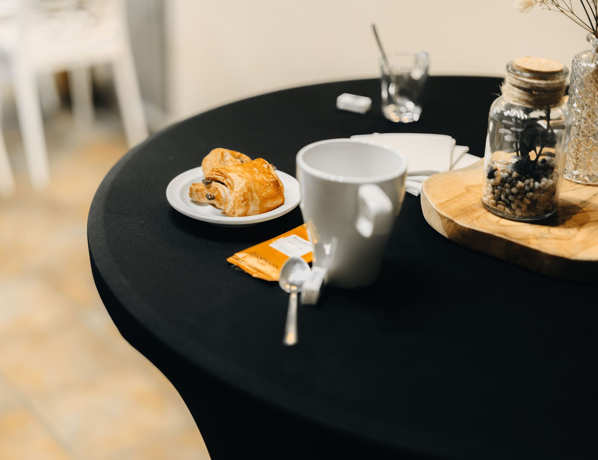 Table ronde noire avec tasse à café, assiette à pâtisserie, serviette, cuillère et centre de table en bocal de verre