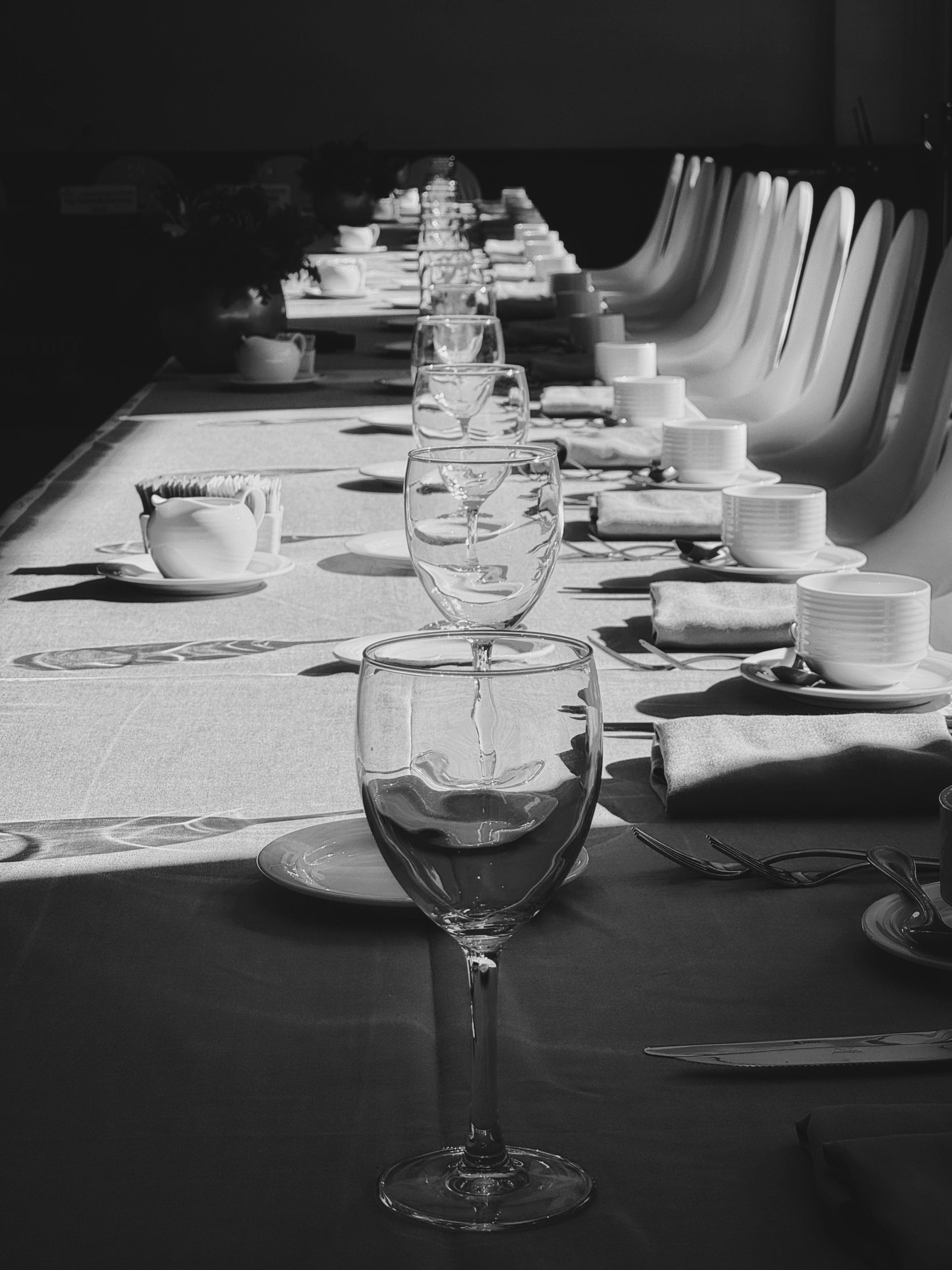Table de banquet en noir et blanc dressée avec verres à vin, tasses et chaises dans une longue salle à manger