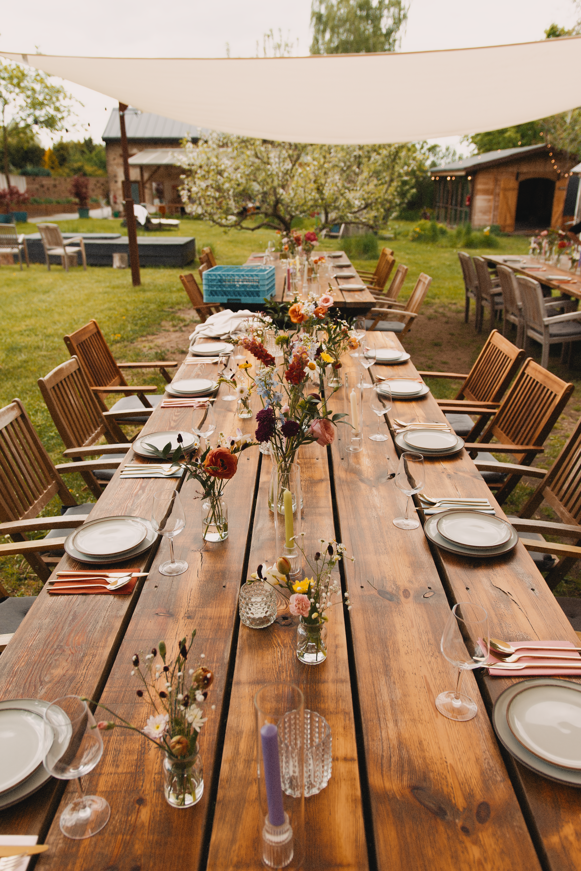 Longue table de jardin rustique dressée pour un repas convivial sous des voiles d'ombrage blanches