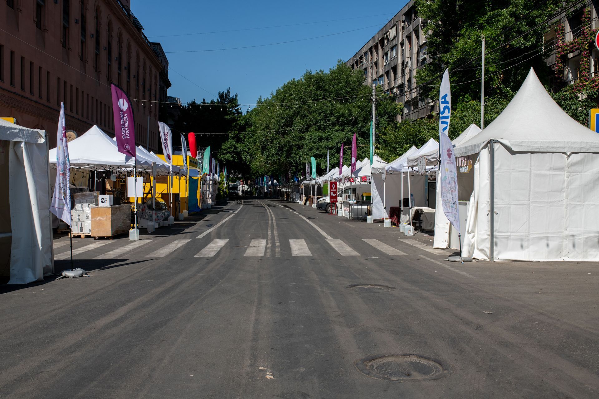 Rue piétonne bordée de tentes blanches et de bannières colorées, abritant un marché en plein air sous un ciel bleu azur.