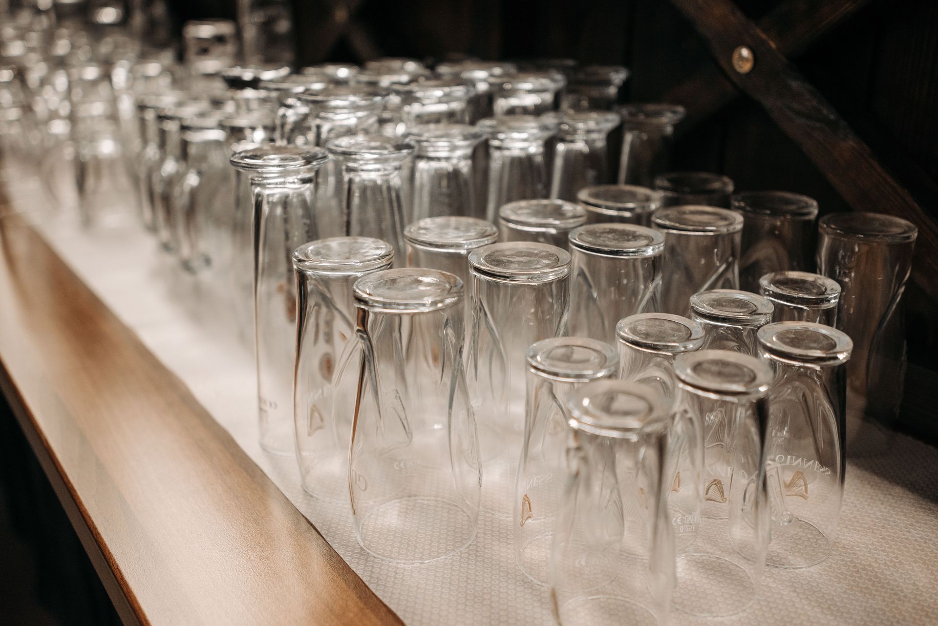 Des rangées de verres transparents renversés sur une serviette blanche à côté d'un comptoir en bois.