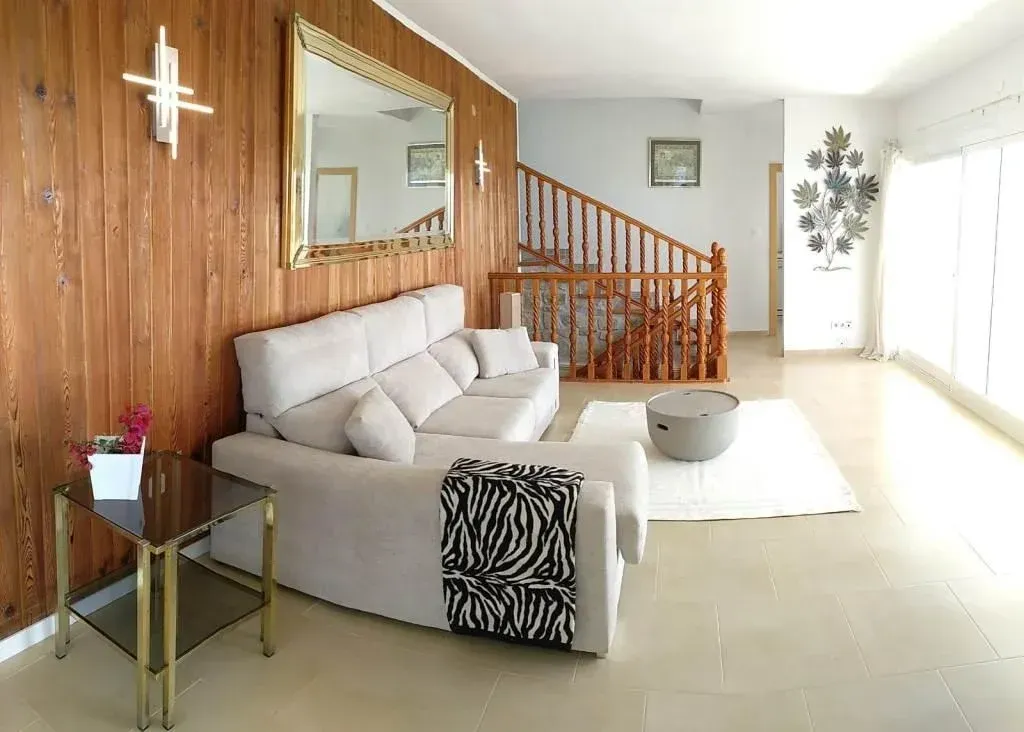 Sala de estar con pared revestida de madera, sofá beige, detalles dorados y una escalera.