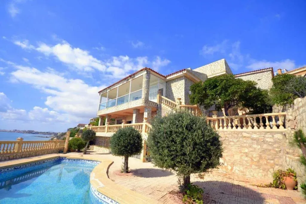 Villa de lujo con piscina con vistas al océano bajo un cielo azul.