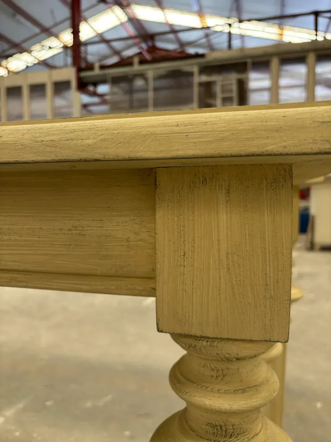 Primer plano de una esquina de mesa de madera de color crema con una pata torneada y detallada.