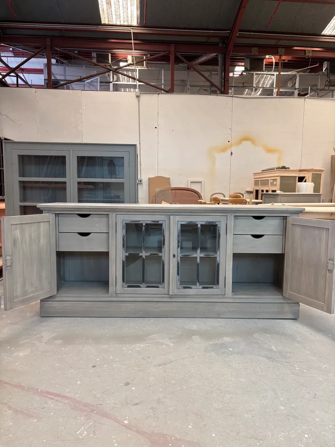 Armario de madera gris con puertas abiertas y cajones en taller.