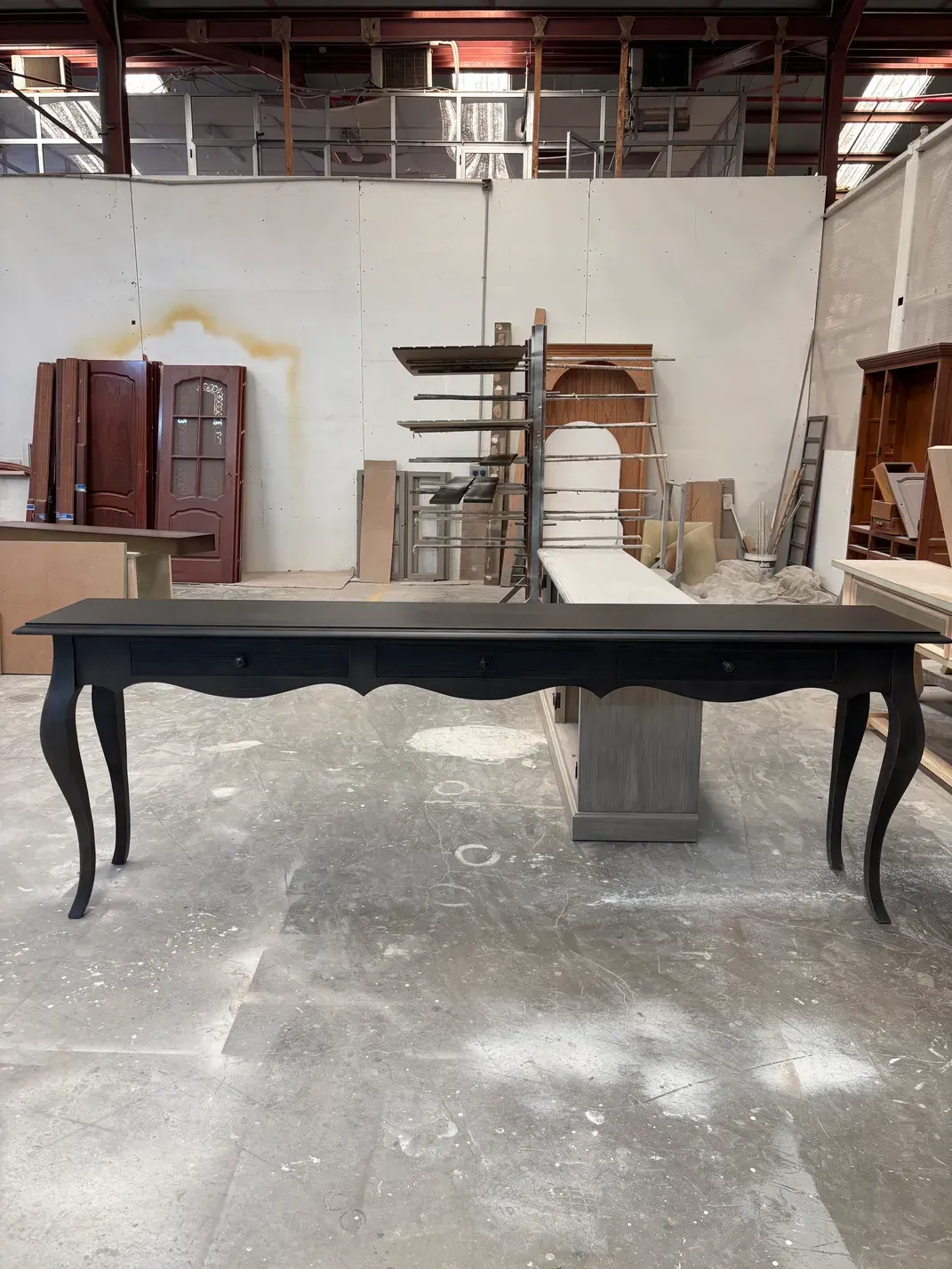 Mesa consola negra con patas curvas en entorno de taller.