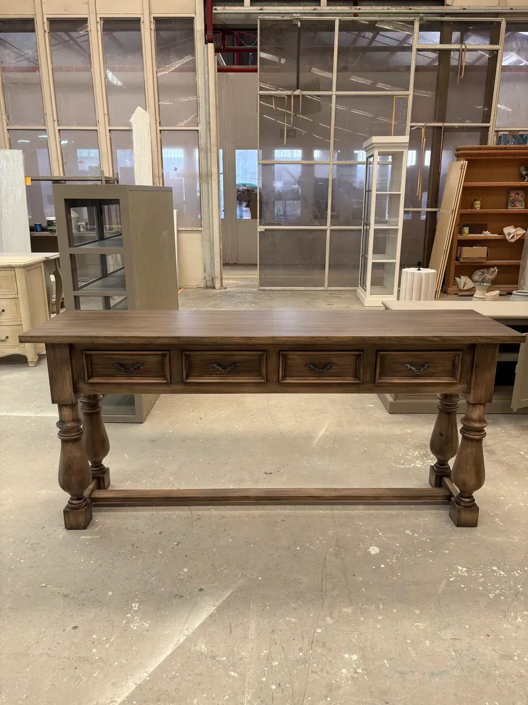 Escritorio de madera con cuatro cajones y patas ornamentadas, en entorno de taller.