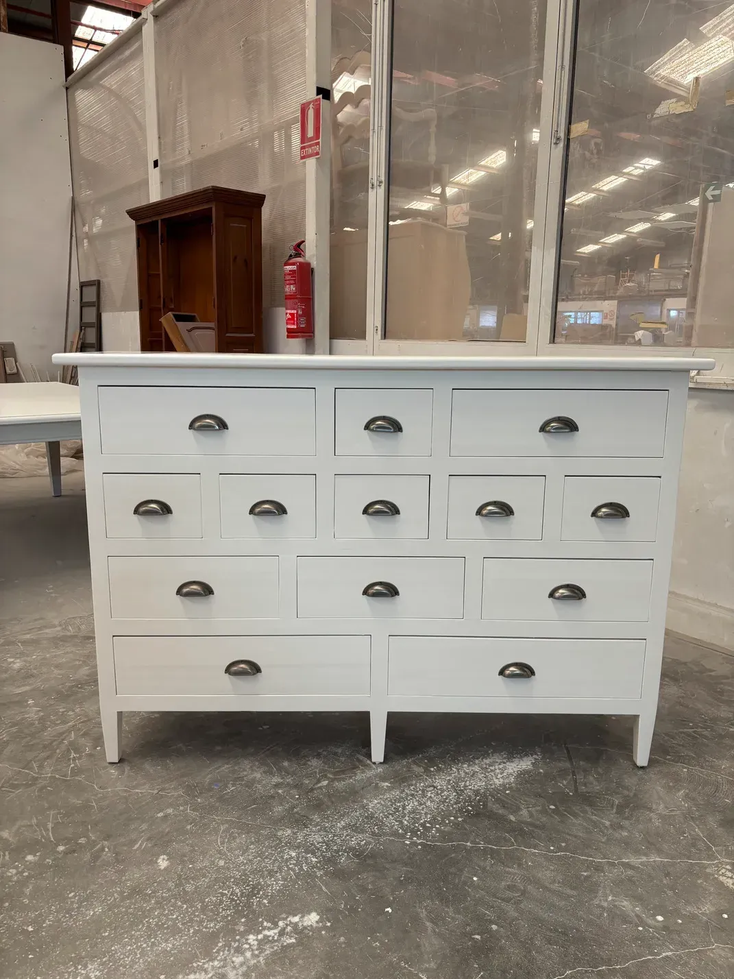 Cómoda blanca con múltiples cajones y tiradores negros, situada en un taller.