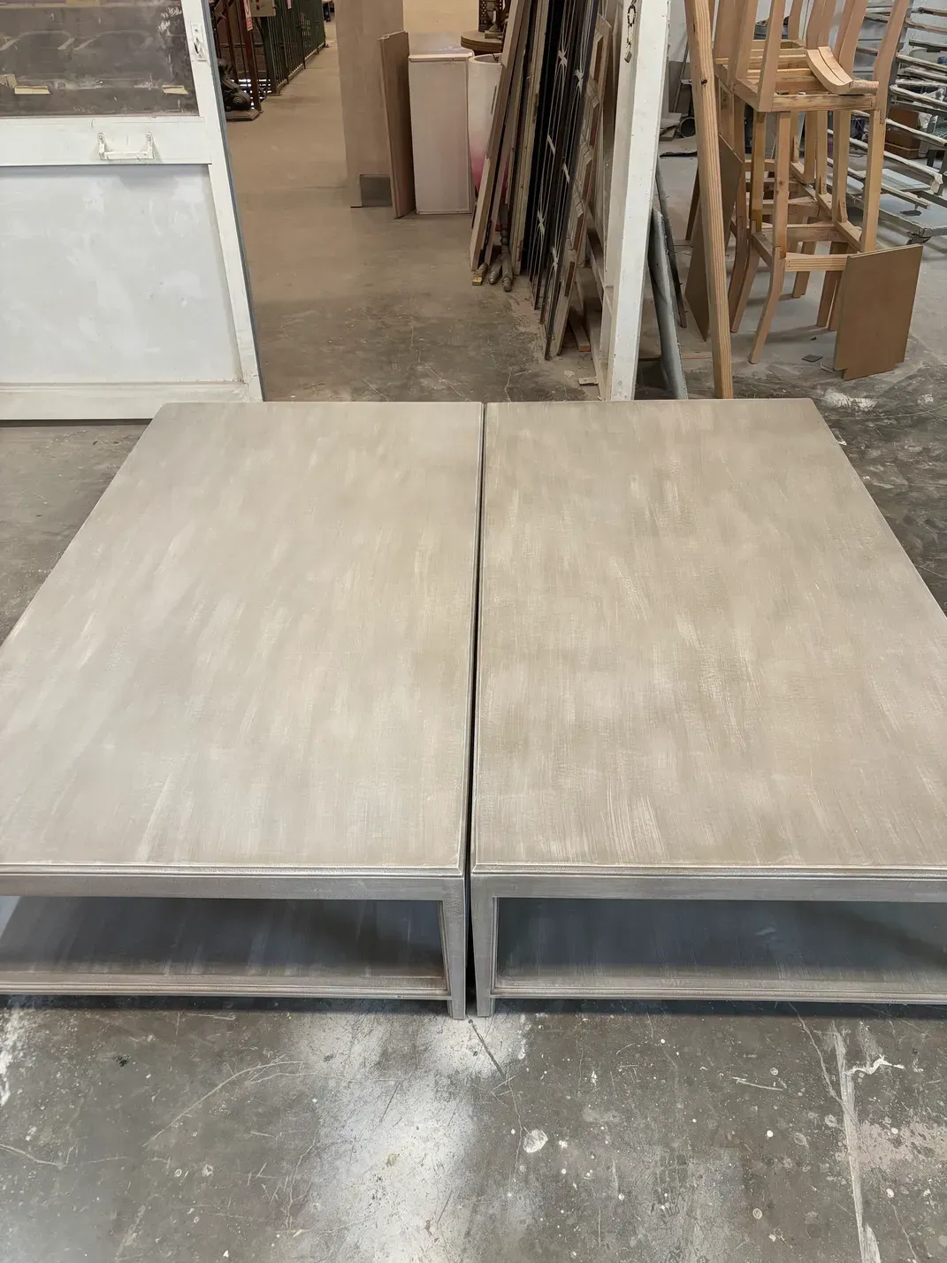 Dos mesas rectangulares de color gris claro con marcos de metal colocadas sobre un suelo de hormigón.