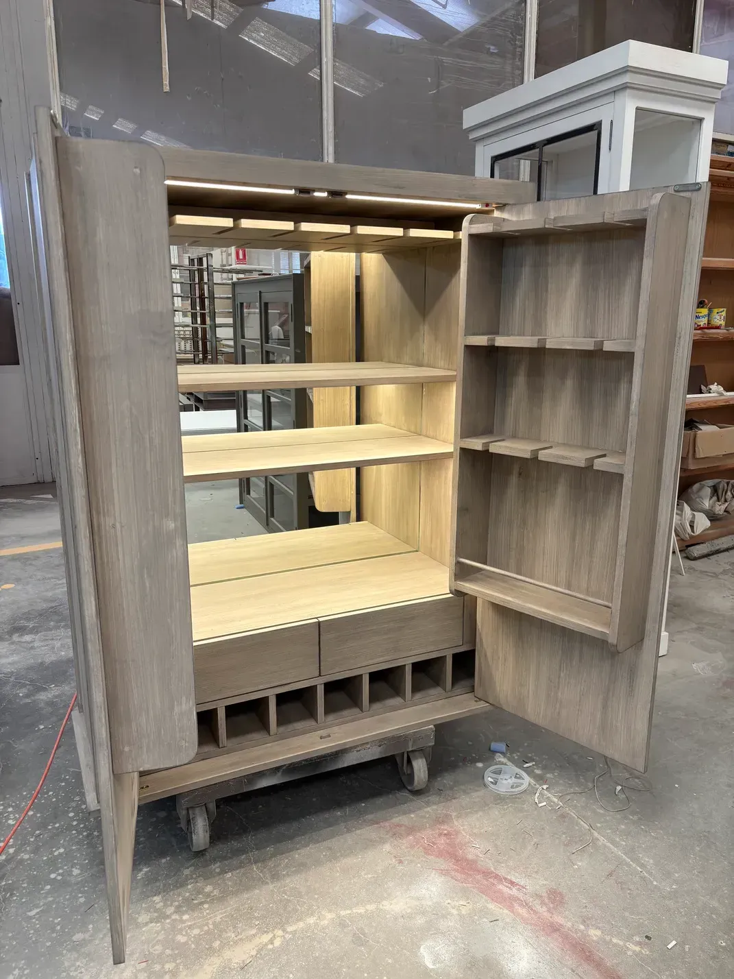 Mueble de madera con puertas abiertas y estantes, botellero para vinos e iluminación interior.