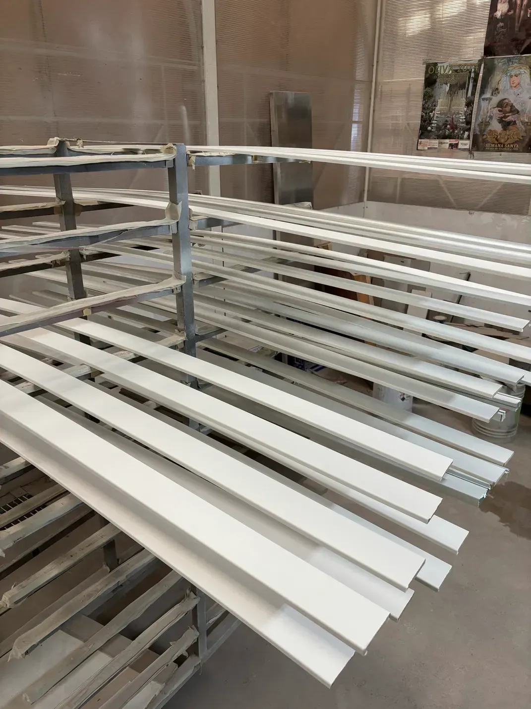 Piezas de madera pintadas de blanco secándose en un estante de metal en un taller.