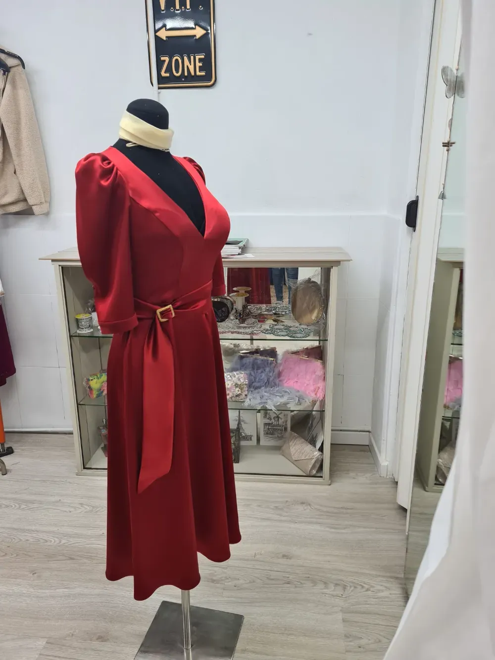 Vestido rojo sobre un maniquí en una tienda de ropa, con una hebilla de cinturón dorada y una bufanda color crema.