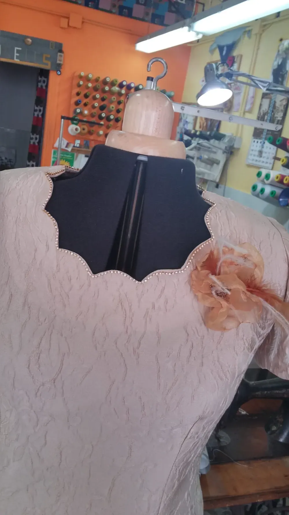 Maniquí en una sastrería exhibiendo un vestido rosa claro con cuello decorativo y detalle floral.