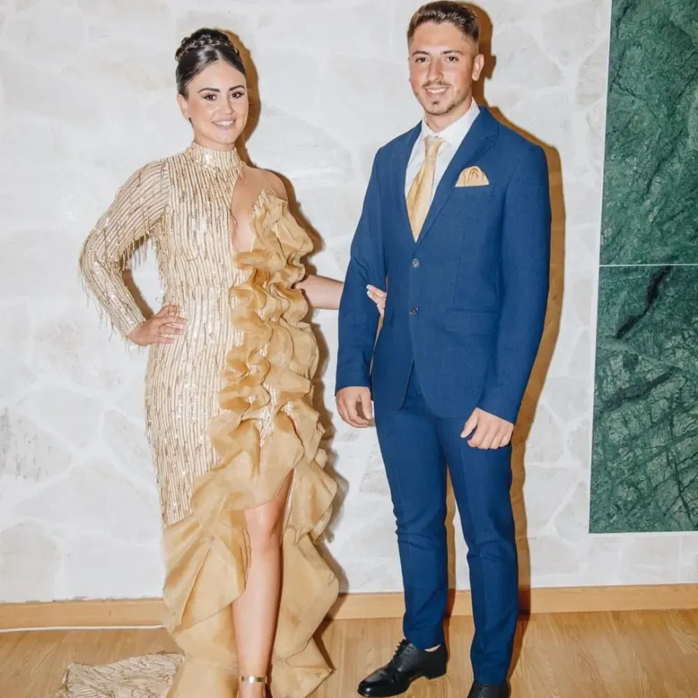 Una mujer con un vestido dorado posa con un hombre con un traje azul.