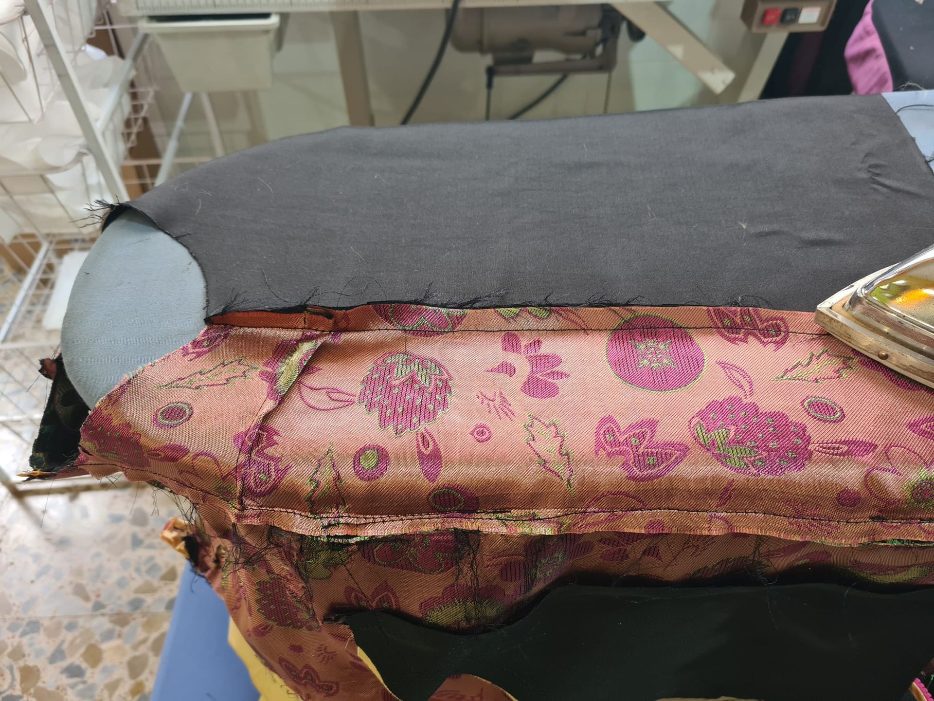 Un primer plano de una tela oscura sobre un cojín estampado que se está planchando. El entorno es una sala de costura.