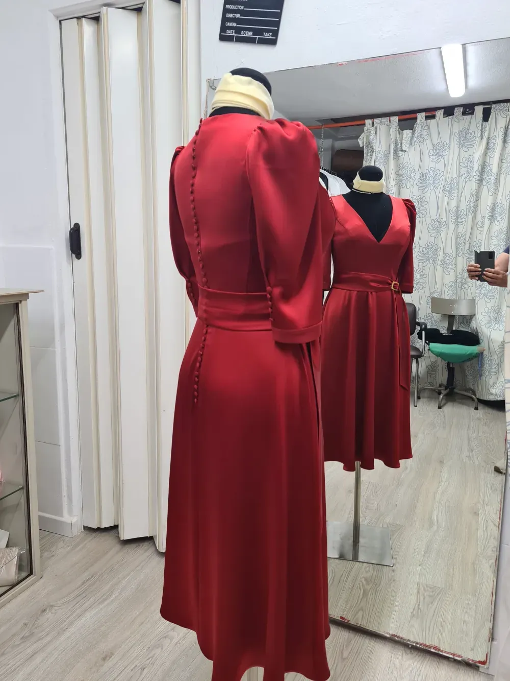 Vestido de satén rojo sobre maniquí, mangas tres cuartos, botones en la espalda, lazo en la cintura, reflejado en el espejo.