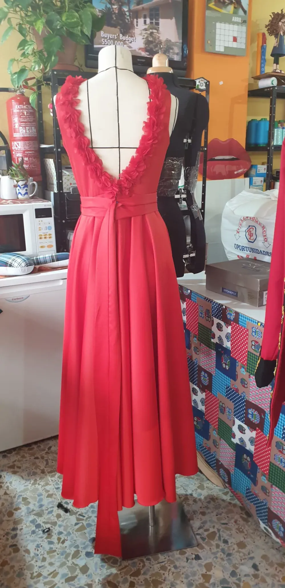 Vestido rojo sobre un maniquí en una habitación con materiales de costura, centrándose en la espalda abierta y la falda suelta.