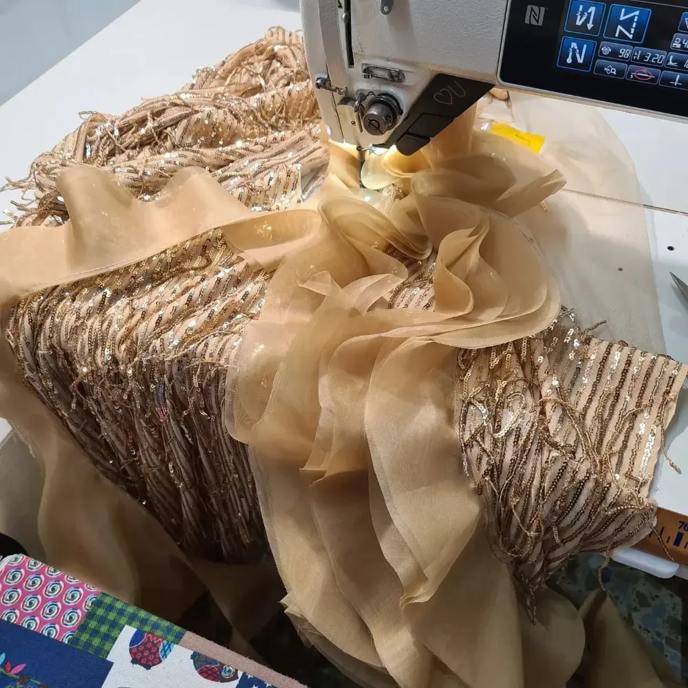 Máquina de coser cosiendo tela beige con flecos y detalles en capas.