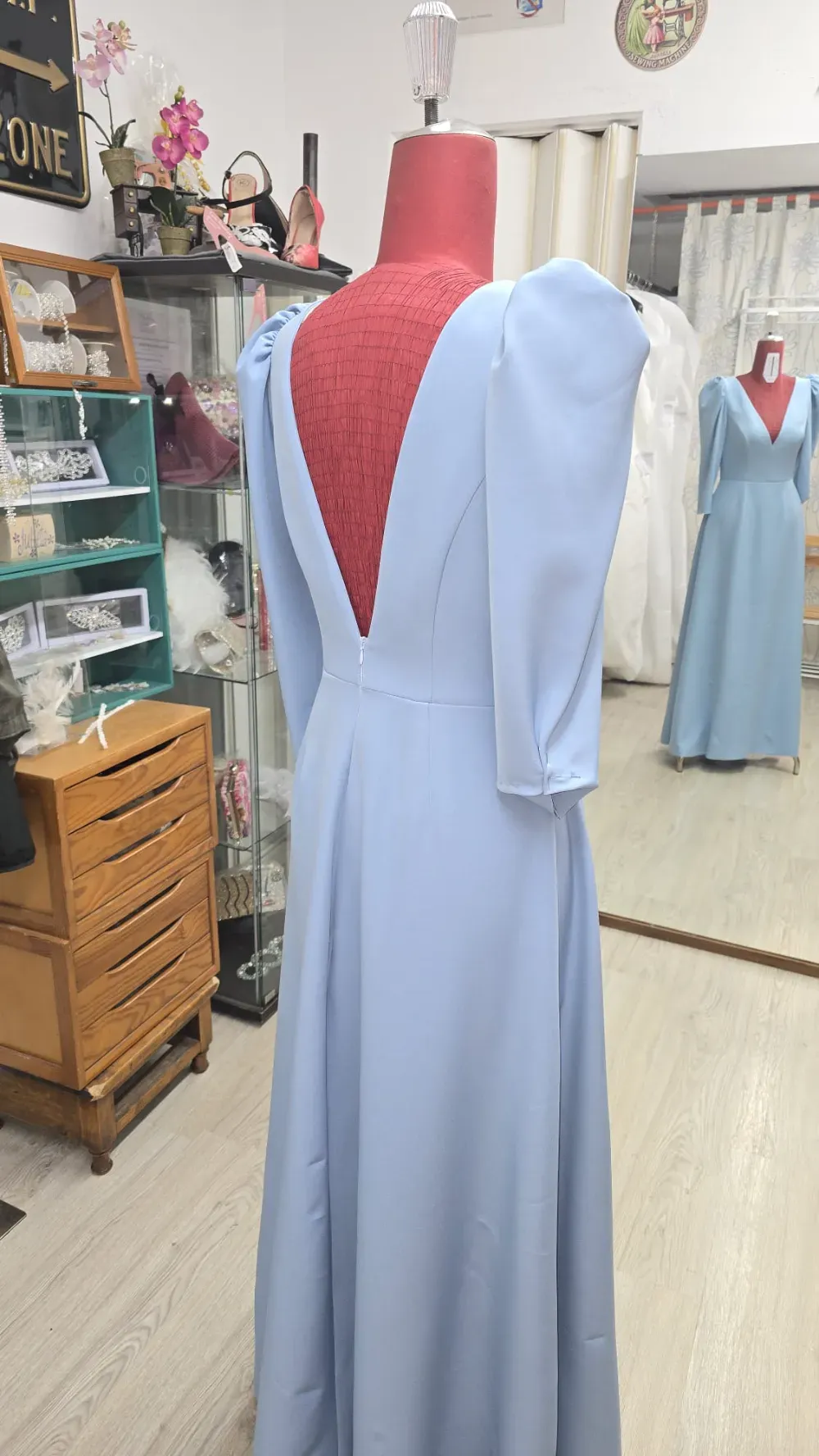 Un vestido azul claro sobre un maniquí con espalda baja, exhibido en un entorno boutique.