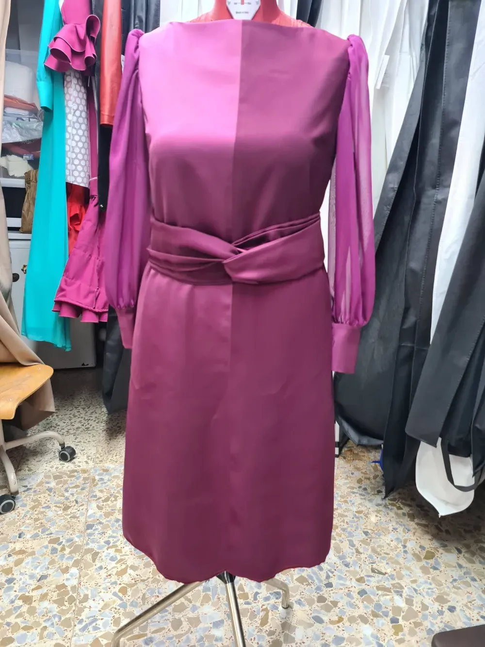 Vestido de satén morado sobre maniquí con mangas transparentes y cinturón retorcido.