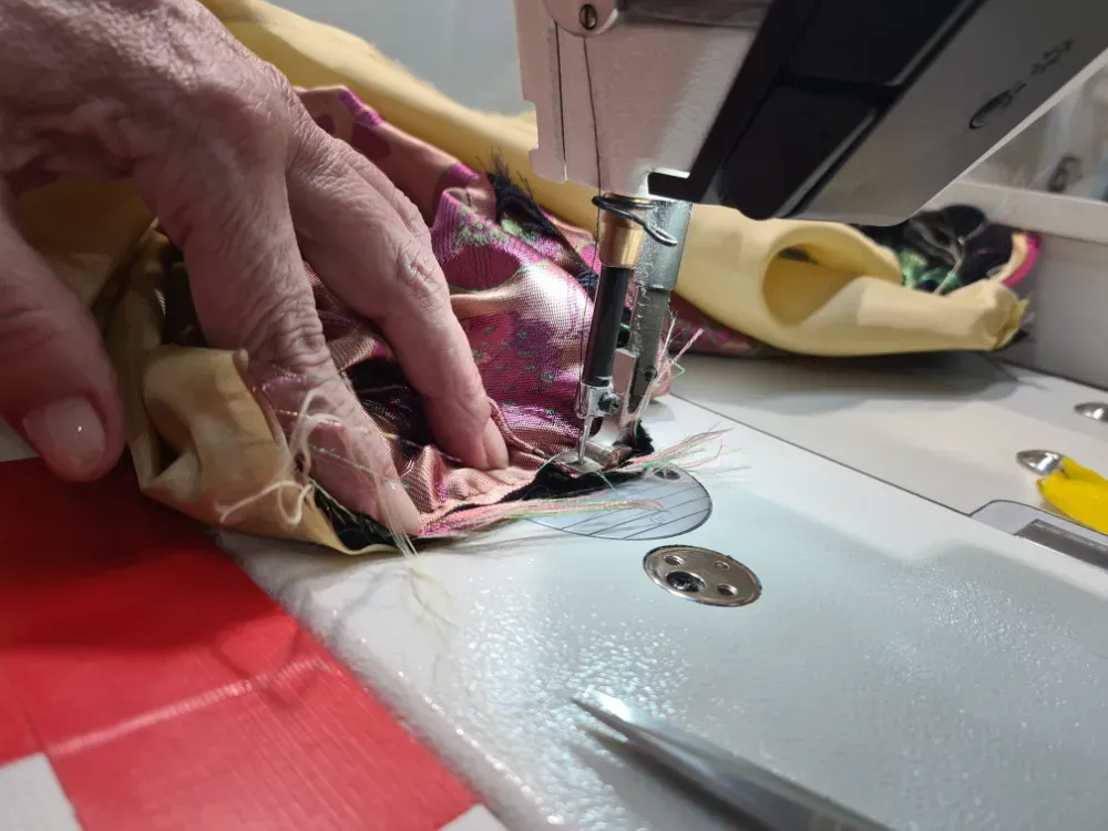 Manos de una persona cosiendo tela con una máquina de coser. Se ven telas de diferentes colores.