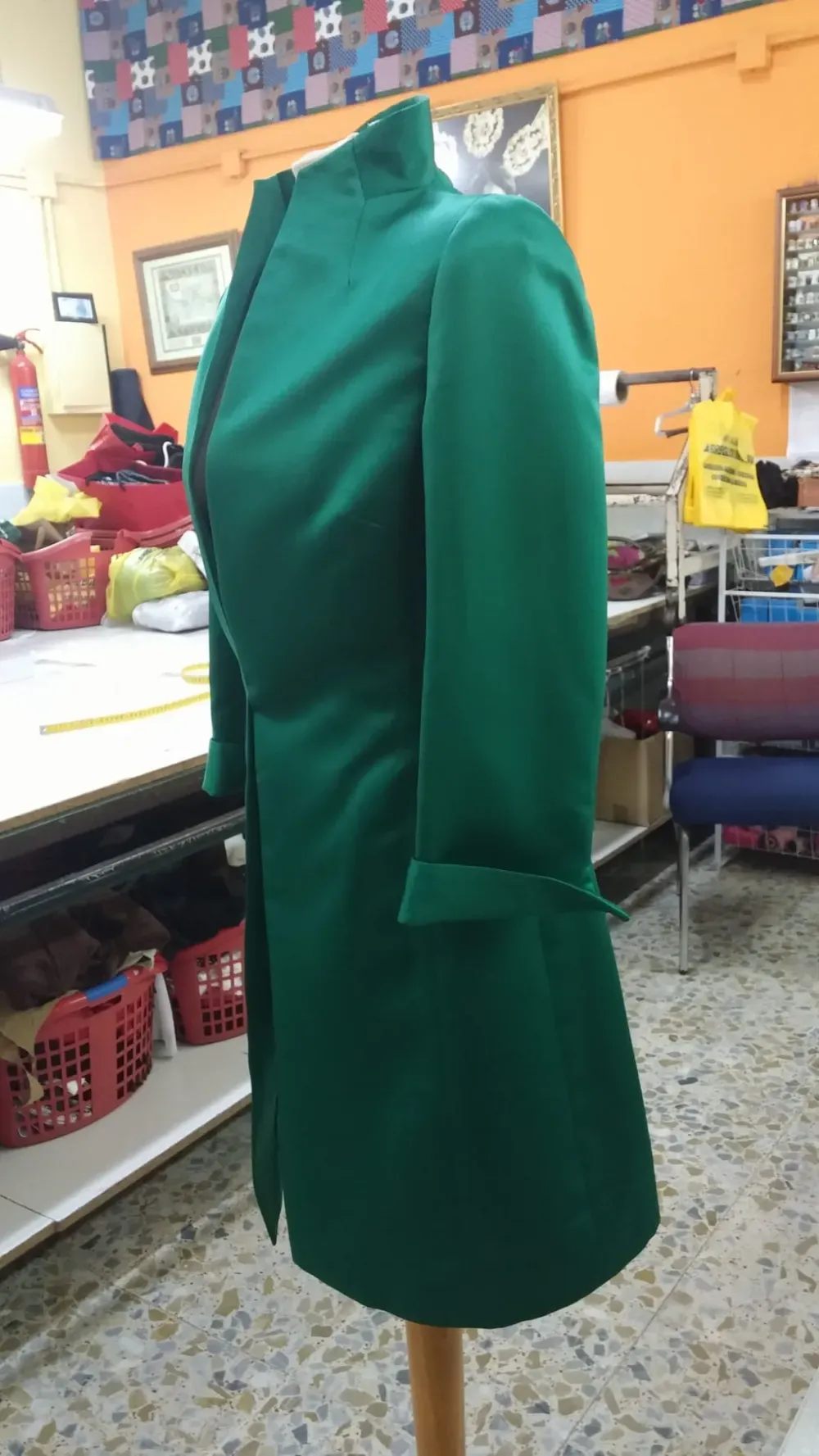 Abrigo verde esmeralda exhibido en un maniquí de madera en un entorno de taller.