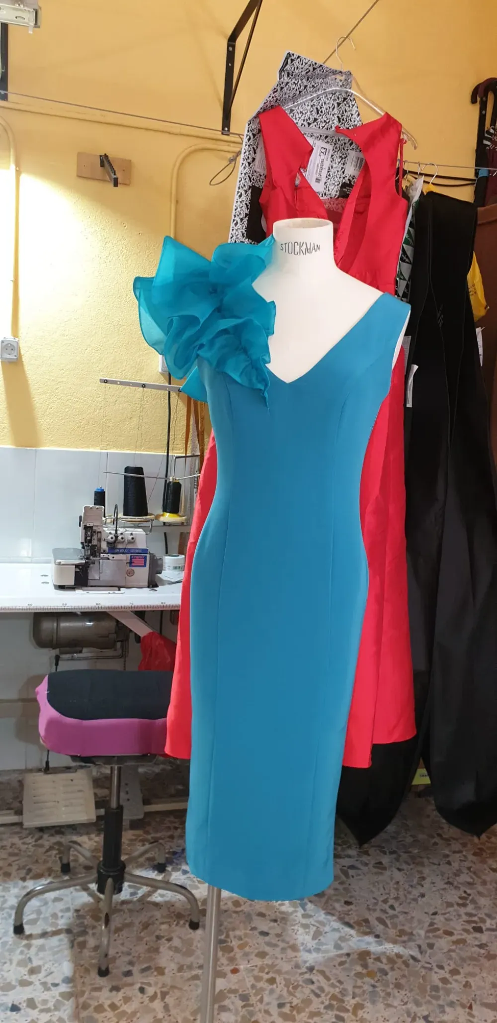 Un vestido azul con un gran detalle de volantes color aguamarina en un hombro, sobre un maniquí en un taller.