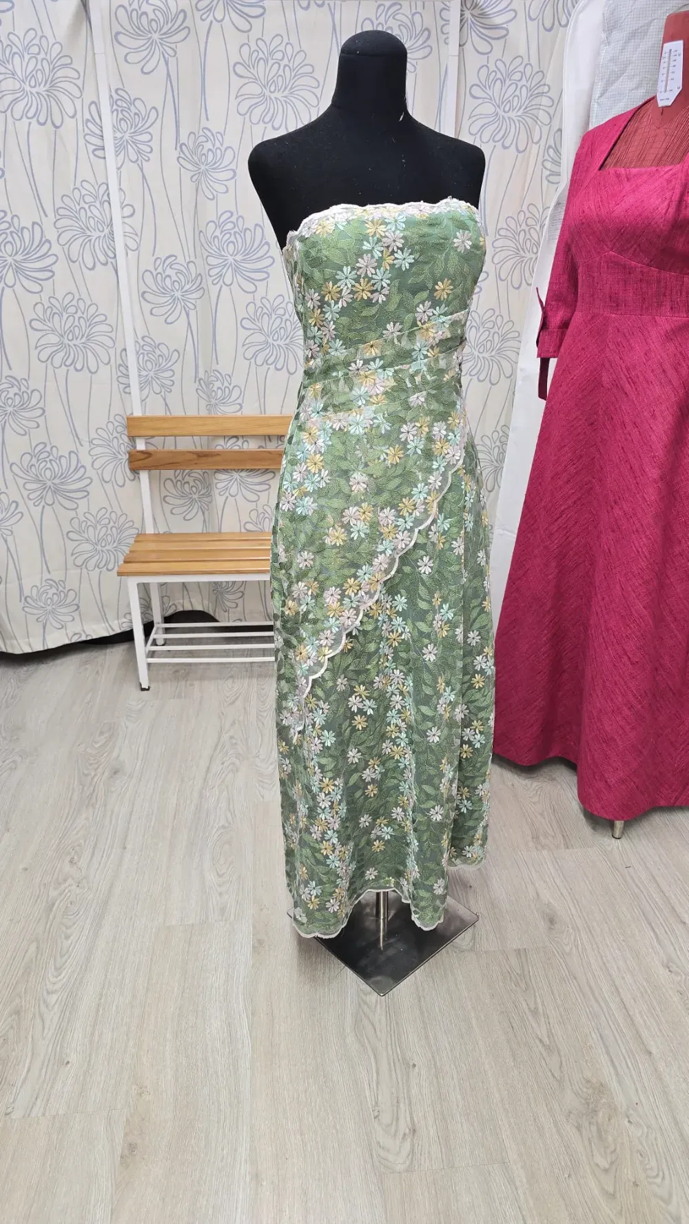 Vestido verde floral sin tirantes sobre un maniquí en una tienda. Ribete de encaje blanco y suelo de madera.