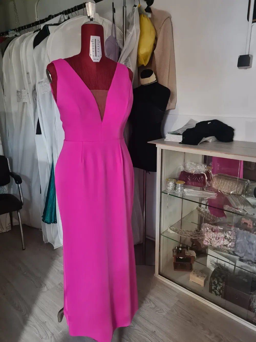 Un vestido formal de color magenta en un maniquí en una tienda de ropa, con otras prendas visibles en el fondo.