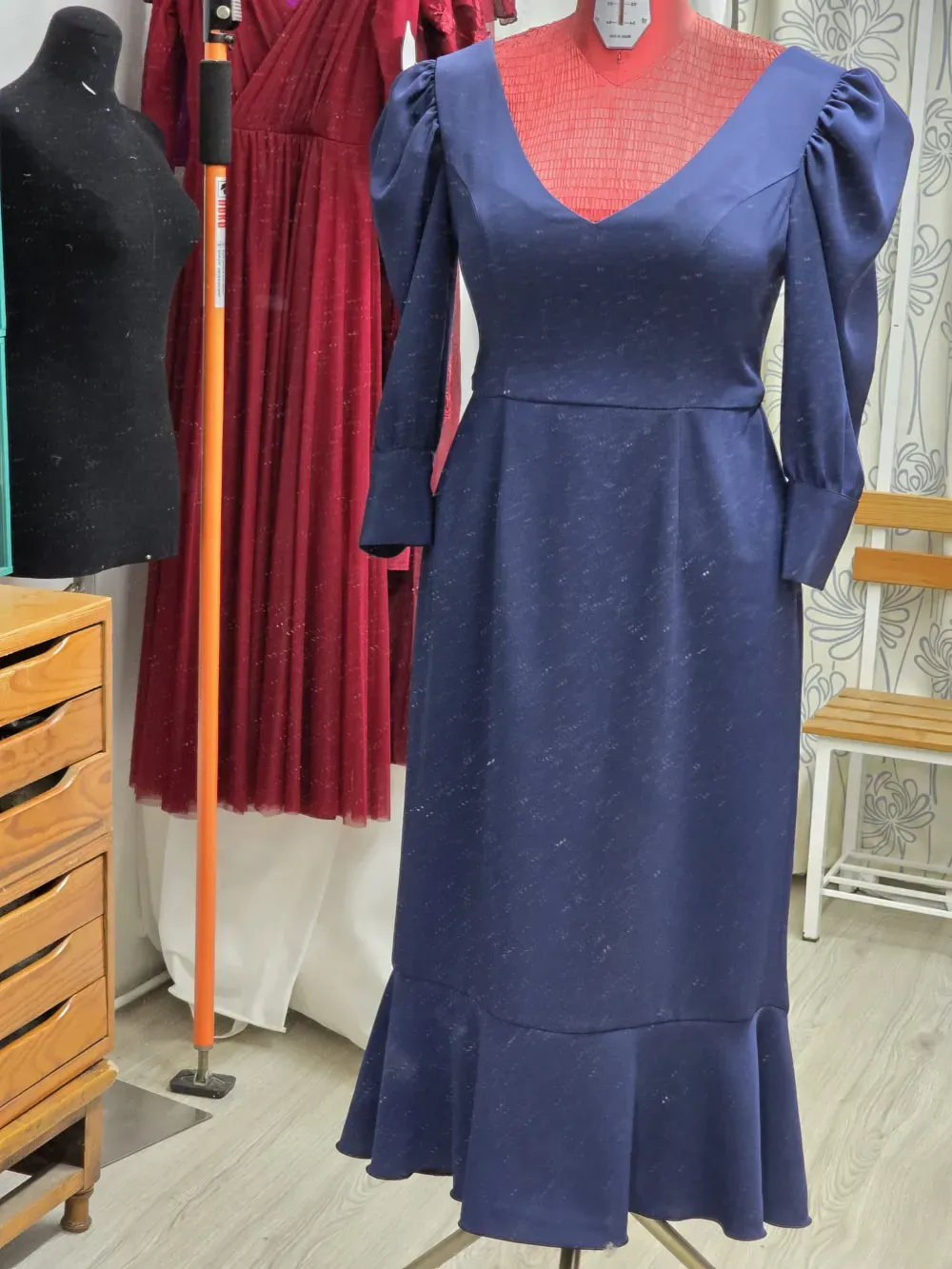 Un vestido azul oscuro con mangas abullonadas exhibido en un maniquí en un taller de costura.