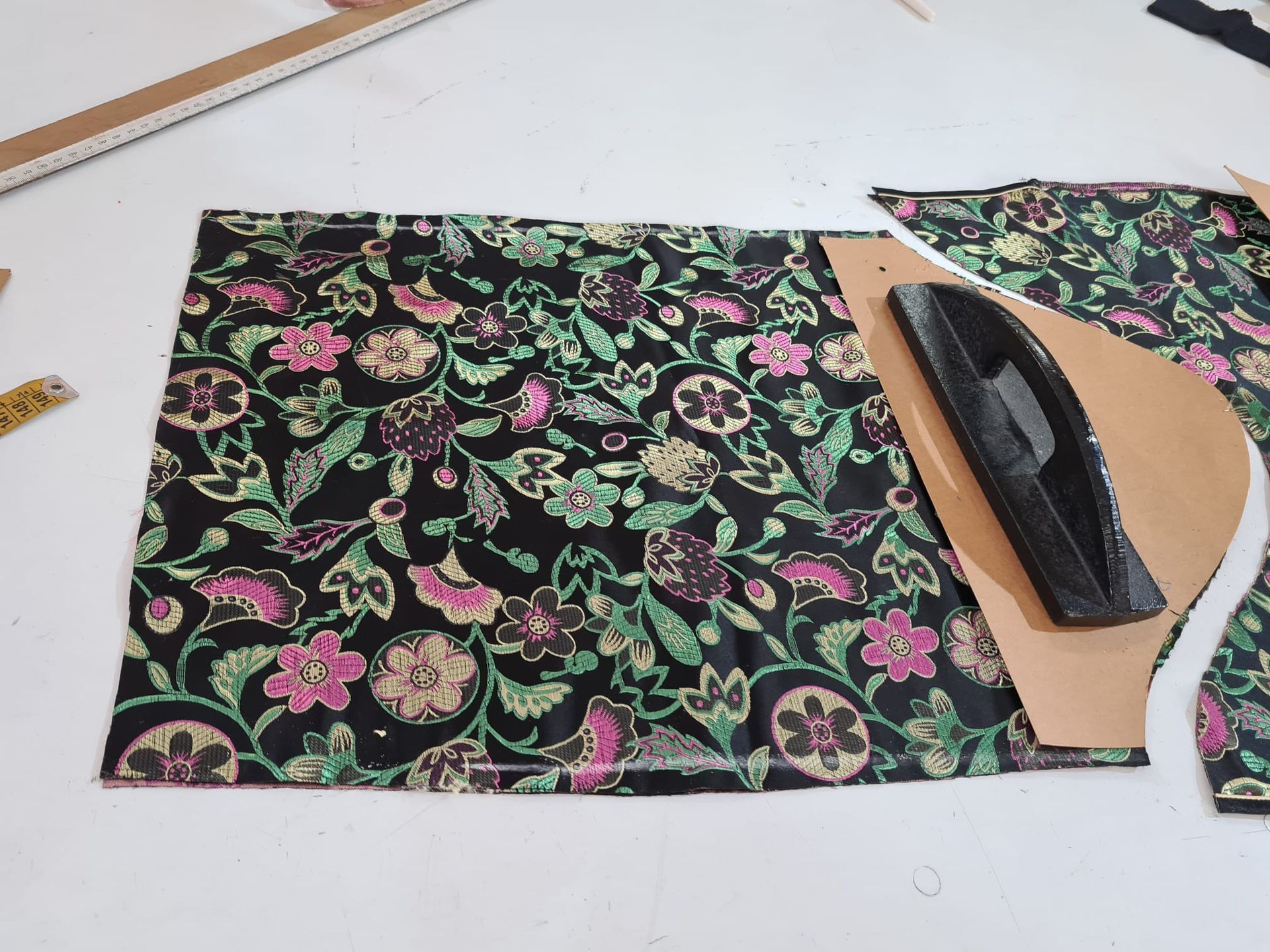 Tela floral negra con estampado y plantilla de cartón con plancha oscura sobre superficie blanca.