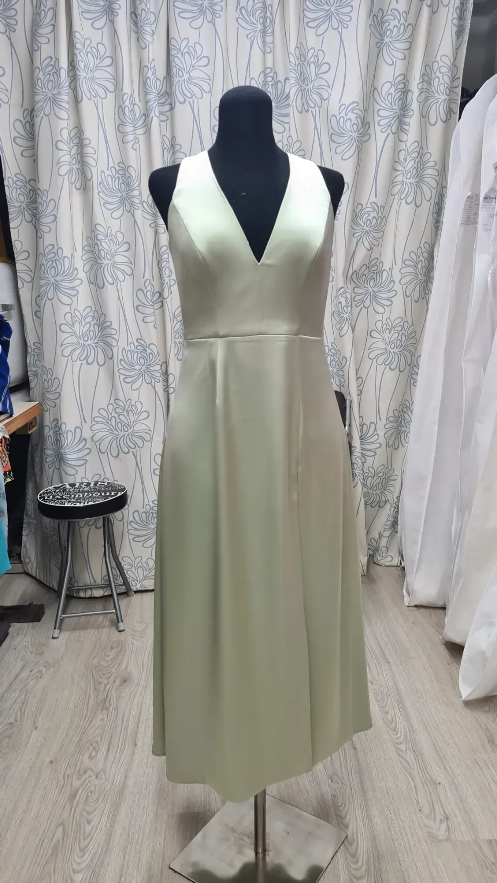 Vestido midi de satén verde claro sobre maniquí negro; escote en pico, sin mangas.