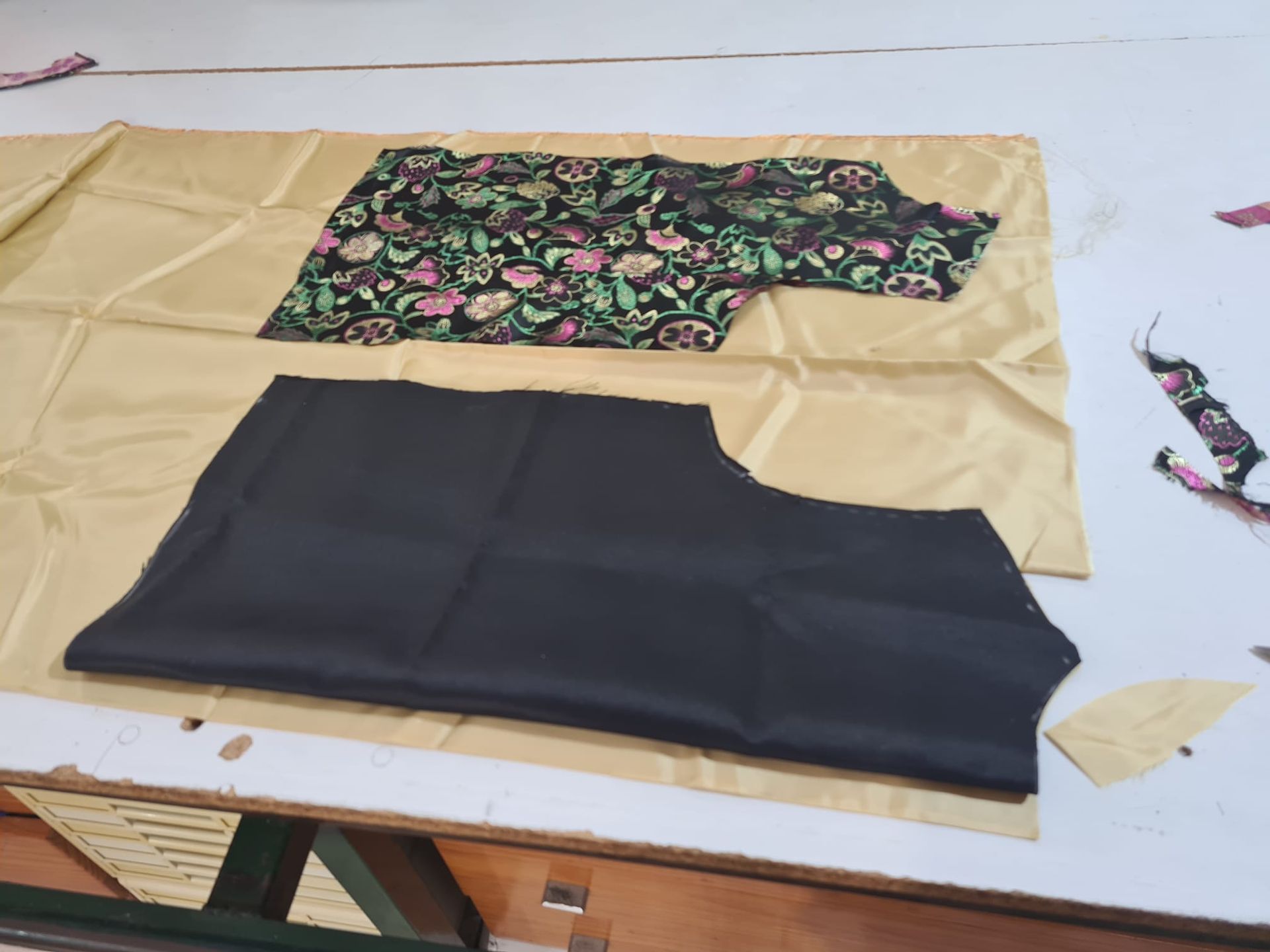 Piezas de tela: un top floral, un corpiño negro y tela dorada sobre una mesa blanca.