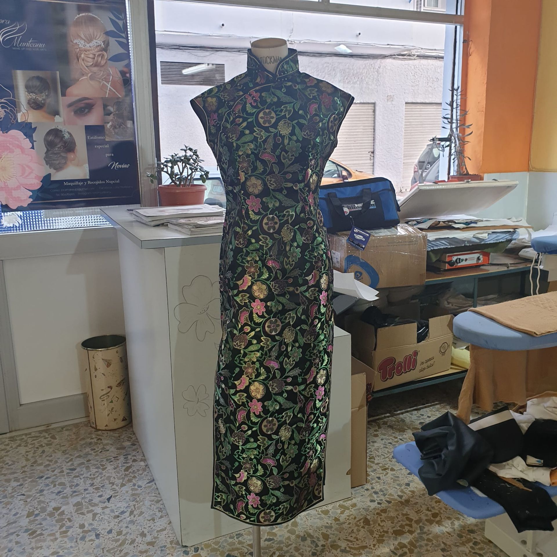 Vestido cheongsam con estampado floral negro sobre un maniquí en una habitación desordenada.