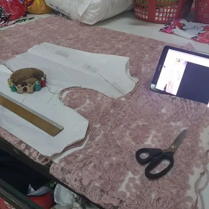 Espacio de trabajo de costura con tela, patrones, tableta que muestra video, tijeras, alfileres y regla.