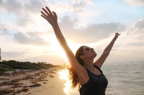 Frau am Strand mit erhobenen Armen, dem Gesicht zur Sonne.